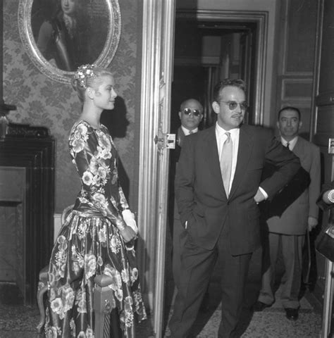 A Man In A Suit And Tie Standing Next To A Woman In A Floral Dress