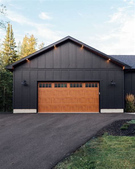 A Black Garage With Two Brown Doors And Lights On The Windows Is Shown