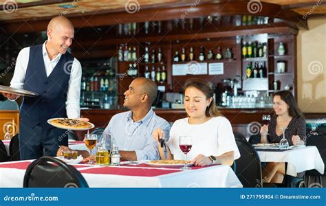 Mesero Educado Sirviendo Pizza A Pareja Hispana En El Restaurante Foto