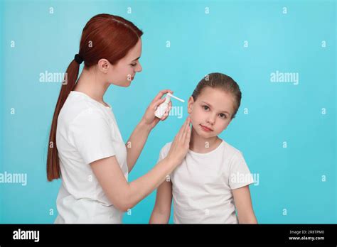 Mother Spraying Medication Into Daughters Ear On Light Blue Background