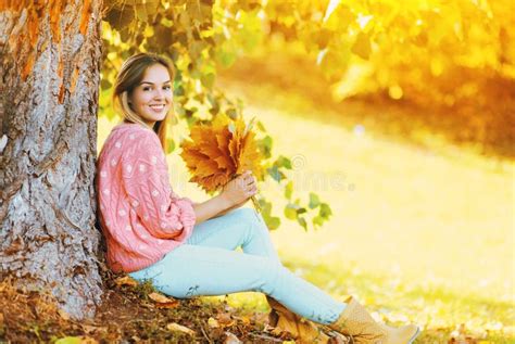 Happy Smiling Woman With Yellow Maple Leafs Sitting Under Tree In Sunny