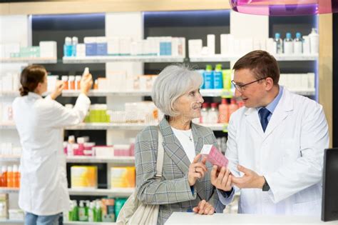 Middle Aged Male Pharmacist Consulting Old Woman Costumer About Care