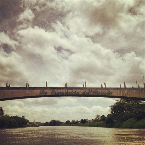 A Bridge That Has Some Writing On It And Is Over Water With Clouds In