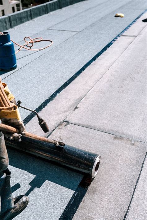 Workers Waterproofing Flat Concrete Roof Using Blowtorch And Bituminous