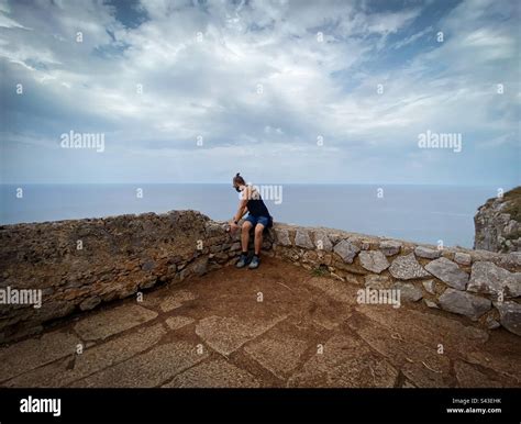 Man Sitting On Stone Wall Looking Over Cliff Stock Photo Alamy