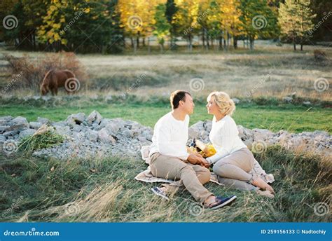 Man And Woman Sitting On A Blanket On The Lawn Holding Hands Stock