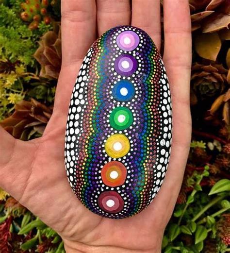 A Hand Holding A Painted Rock In Front Of Some Plants