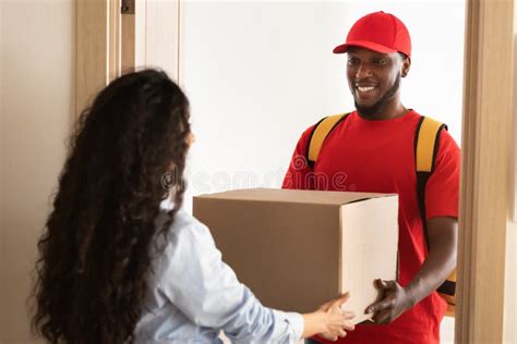 Black Delivery Man Giving Box To Woman Standing At Door Stock Image