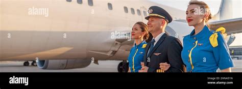 Excited Male Pilot Walking Together With Two Flight Attendants In Blue