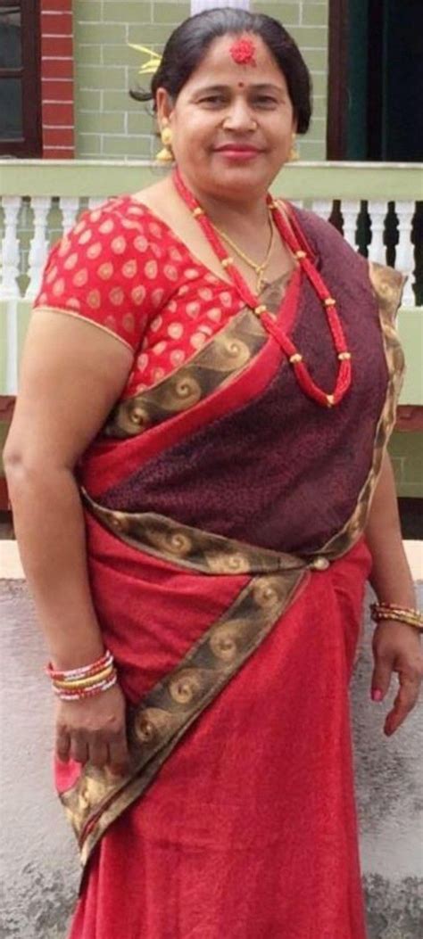 A Woman In A Red And Gold Sari Standing Next To A White Fence With Her Hands On Her Hips