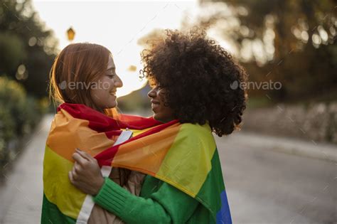 Multiracial Lesbian Couple Look At Each Other With Love Embracing With The Lgbt Rainbow Flag