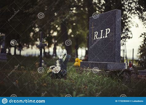 Single Tombstone With Rip Sign In Old Graveyard Close Up Of Gravestone In Grass With Flower And