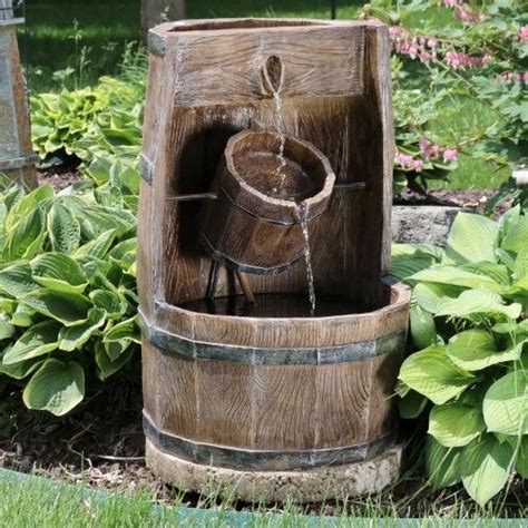 A Wooden Barrel Fountain In The Middle Of A Garden With Flowers And