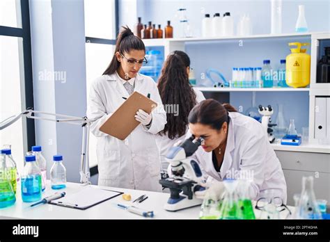 Three Woman Scientists Using Microscope Write On Checklist At