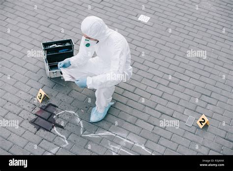 Male Criminologist In Protective Suit And Latex Gloves Explore Evidence