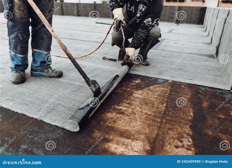 Workers Waterproofing Flat Concrete Roof Using Blowtorch And Bituminous