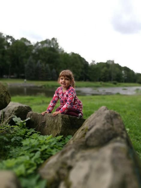 Premium Photo Portrait Of Smiling Girl Sitting On Rock Formation By