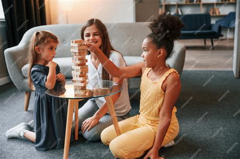 Premium Photo Sitting On The Floor A Young Woman With Two Girls Is Playing A Wooden Tower Game