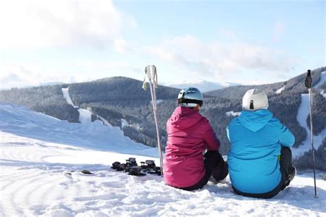 Couple With Ski Equipment Sitting On Snowy Hill In Mountains Space For