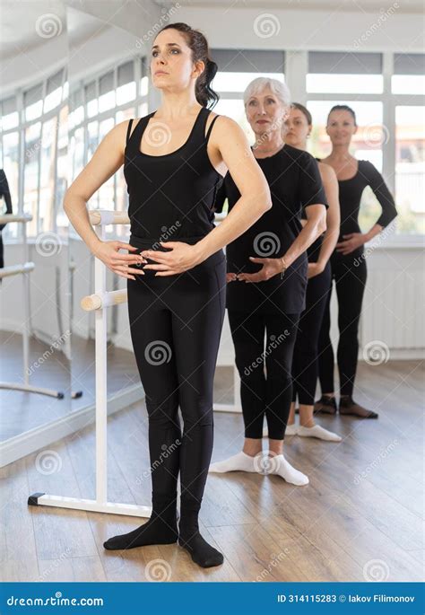 Women Stand In Fifth Position Near Ballet Barre During Group Training