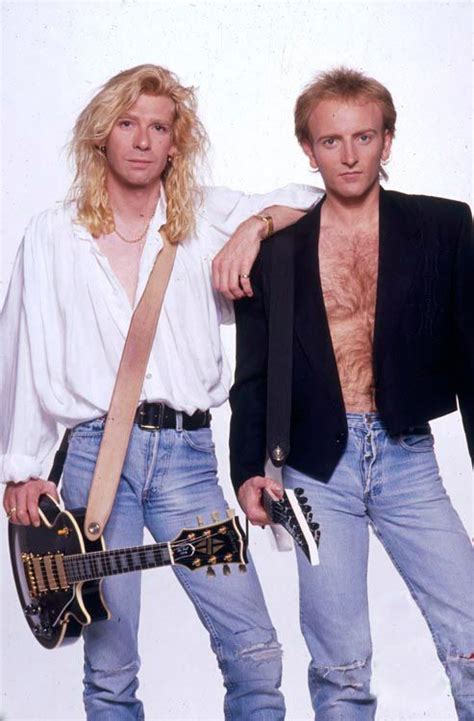 Two Men Standing Next To Each Other Holding Guitars