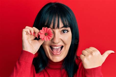 Young Hispanic Woman Holding Sunflower Over Eye Pointing Thumb Up To