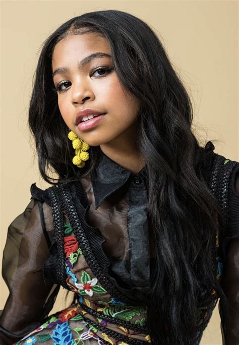 A Woman With Long Black Hair Wearing A Sheer Shirt And Yellow Earring Posing For The Camera