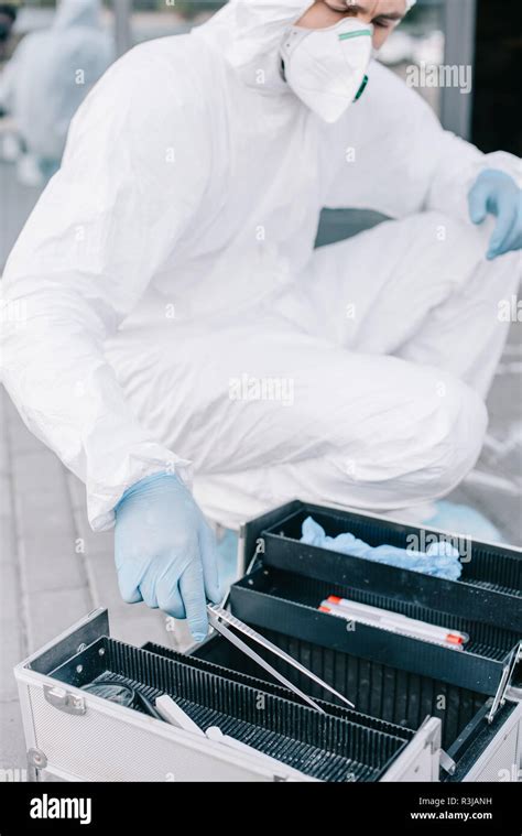 Male Criminologist In Protective Suit And Latex Gloves Taking Tweezers