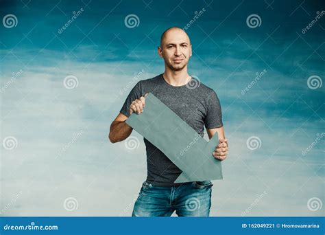 A Tall Bald Man In A Gray T Shirt And Blue Jeans Holds In His Hands A