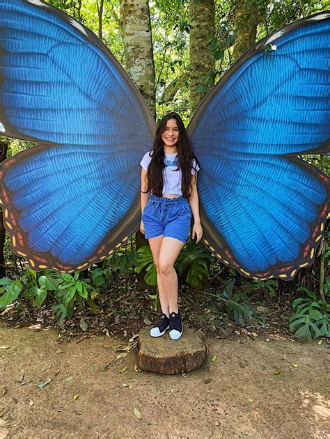 A Woman Standing Next To A Giant Blue Butterfly In The Forest With Her