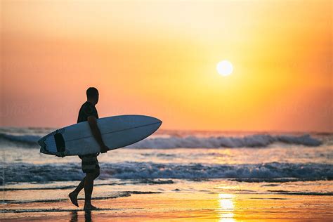 Man Carrying Surfboard Along Beach At Sunset By Stocksy Contributor