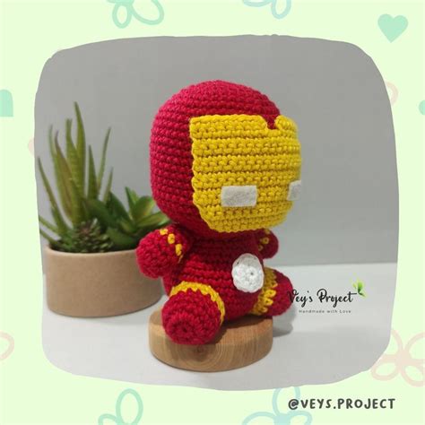 A Crocheted Iron Man Sitting On Top Of A Wooden Stand Next To A Potted