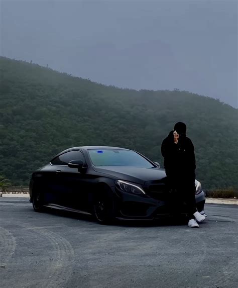 A Man Standing Next To A Black Car On Top Of A Parking Lot With