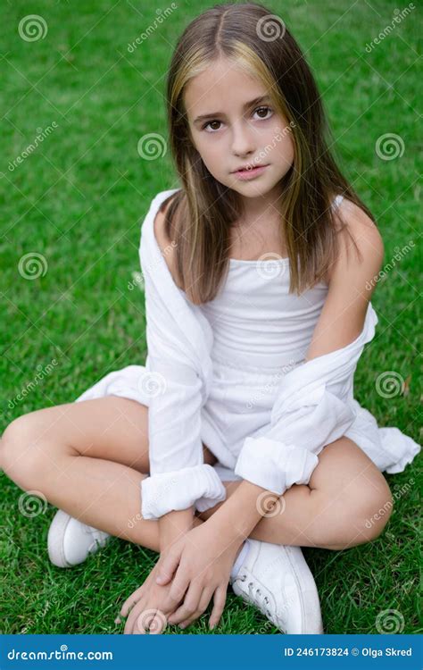 Pretty Tween Girl In White Clothes Sitting On Green Grass Outside In