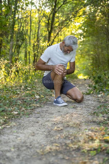 Mature Man Suffering From Knee Pain While Crouching In Forest