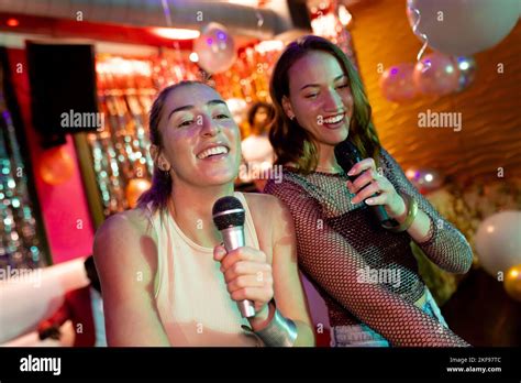 Two Happy Caucasian Female Friends Singing Karaoke At A Nightclub Bar