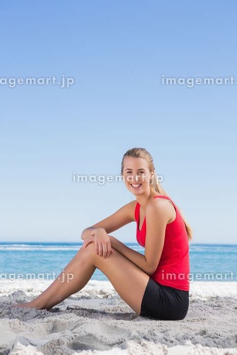 Athletic Blonde Sitting On Sand Smiling At Camera On The Beach