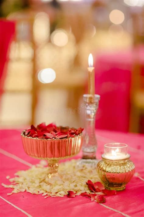 Table Arrangement With A Vase Filled With Flower Petals And Lit Candles