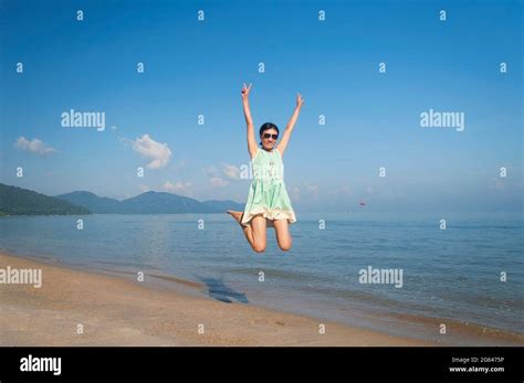 A Beautiful Chinese Woman Flashing Peace Signs Jumping On Long Beach At