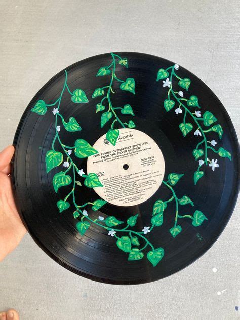 A Hand Holding A Black Record With Green Leaves On It