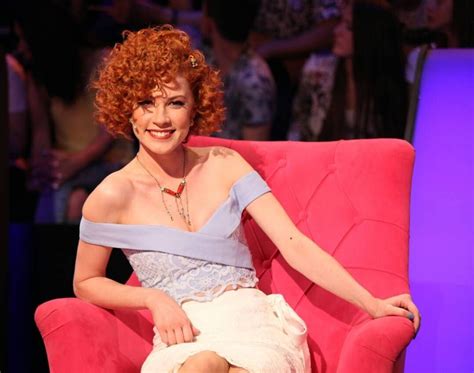 A Woman With Red Hair Is Sitting On A Pink Chair And Smiling At The Camera