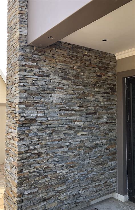 A Large Stone Wall In Front Of A Building With A Black Door And Glass