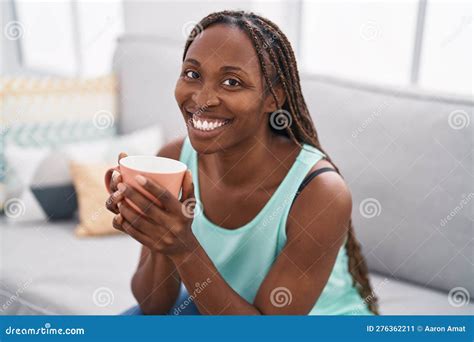 African American Woman Drinking Coffee Sitting On Sofa At Home Stock