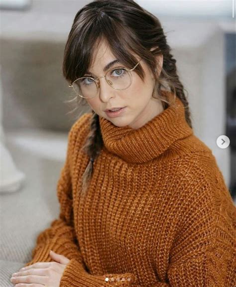 A Woman With Glasses Sitting On A Couch Wearing A Turtle Neck Sweater