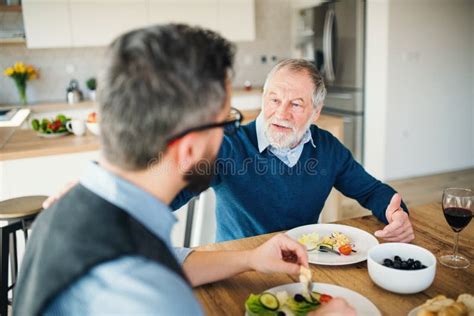 An Adult Hipster Son And Senior Father Indoors At Home Eating Light