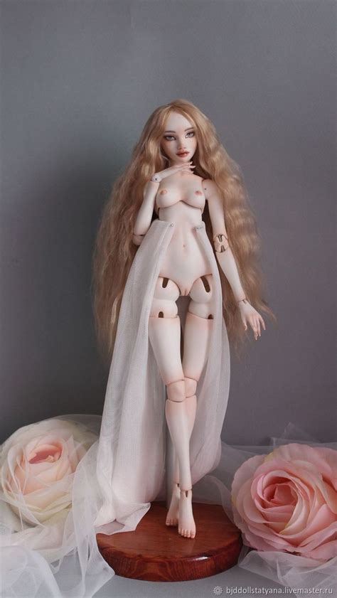 A Naked Doll Sitting On Top Of A Table Next To Pink Roses And Tulle