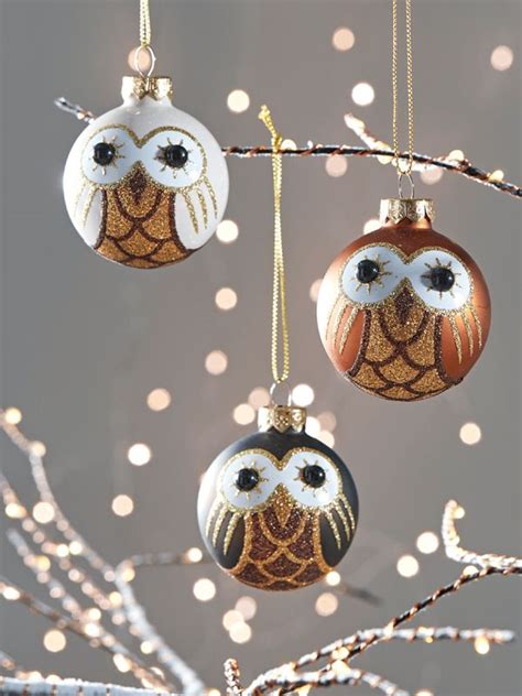 Three Ornaments Hanging From A Tree With Lights In The Background