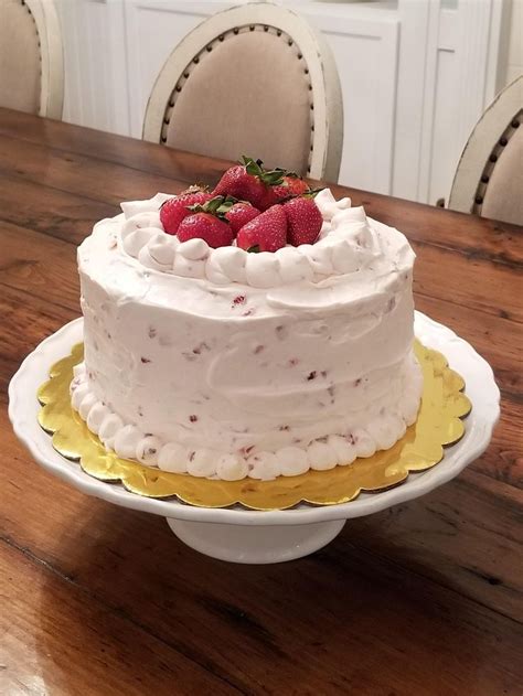 A Cake With White Frosting And Strawberries On Top Sitting On A Table In Front Of Two Chairs