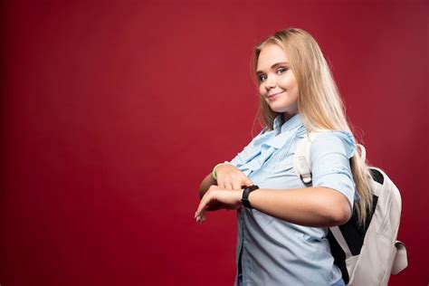 Une jeune étudiante blonde retourne à l école et vérifie l heure sur sa montre Photo Gratuite