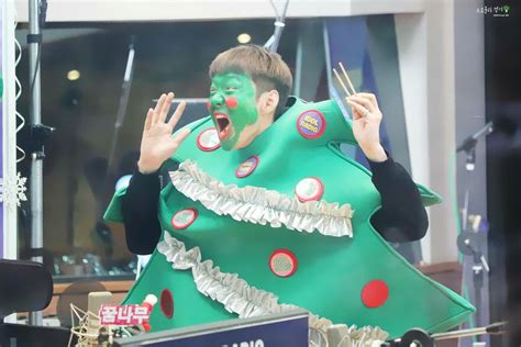 A Man Dressed As A Christmas Tree With His Hands In The Air While